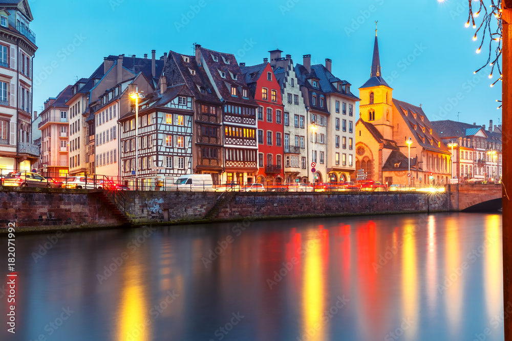 Picturesque Christmas quay and church of Saint Nicolas with mirror reflections in the river Ile during evening blue hour, Strasbourg, Alsace, France