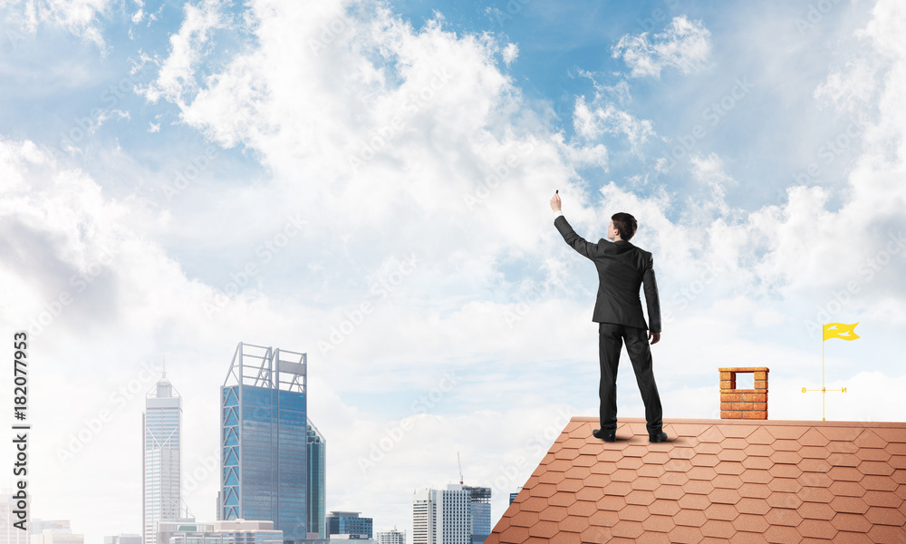 Businessman on house roof touch empty space. Mixed media Businessman on house roof touch empty space. Mixed media