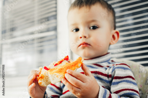 The little boy in the kitchen eating a small pizza