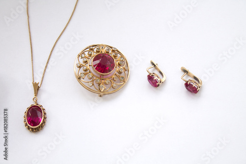 Gold brooch, ear-rings, chainlet with a coulomb with a ruby on a white background, handwork photo