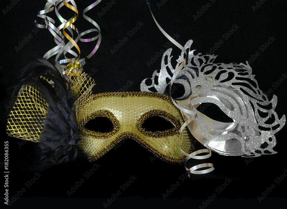 New Year's Eve themed image of gold and silver carnival masks decorated with black flower and feathers with gold ribbons on black background.