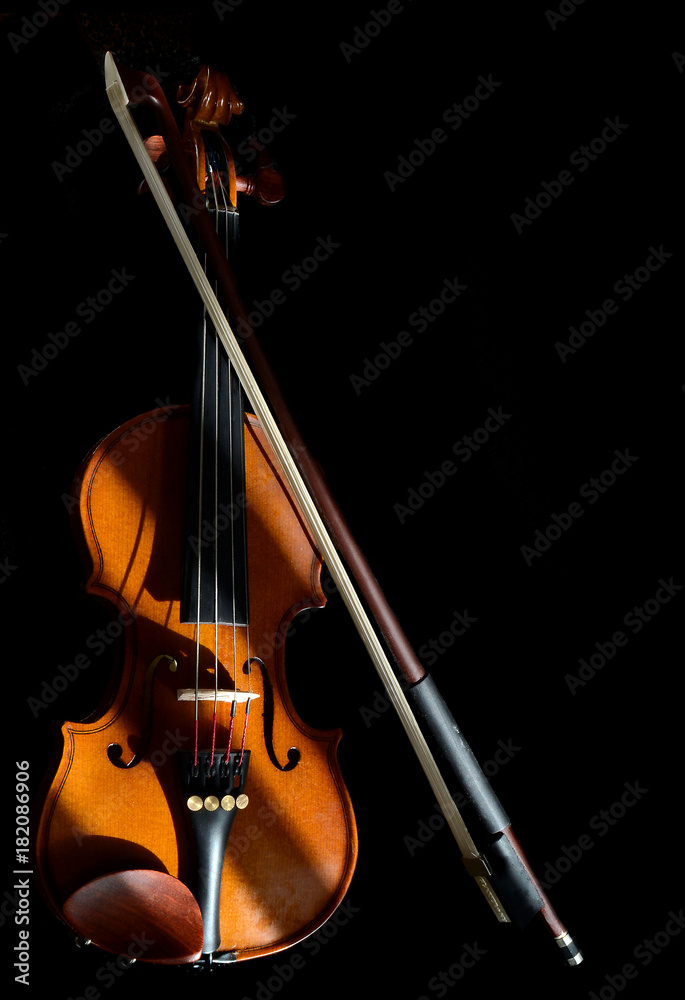 Fototapeta premium Sunshine and shadows play across a miniature violin and bow on black background. Copy space. Vertical composition.
