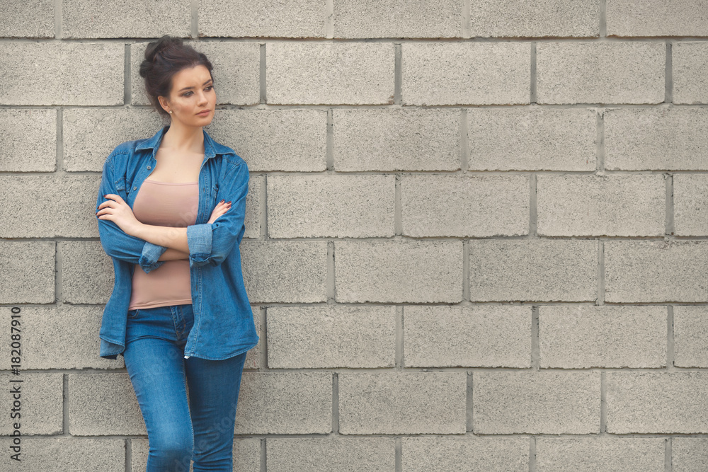 Fashion woman in denim standing near empty brick wall Fashion woman in denim standing near empty brick wall