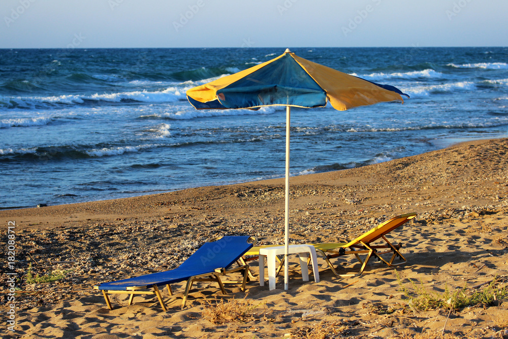 Yellow-blue beach umbrella and sun beds with table on a sandy beach by the sea Yellow-blue beach umbrella and sun beds with table on a sandy beach by the sea
