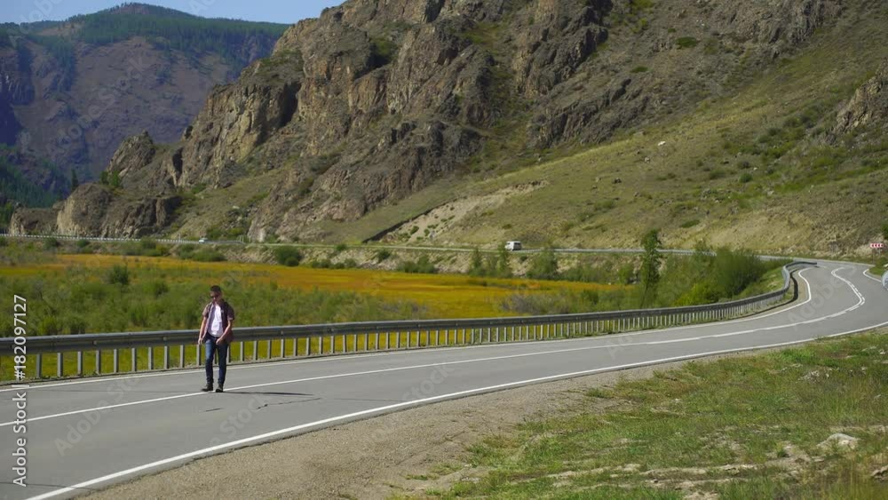 Young traveler man with backpack walking alone on the road on the mountain. Hitchhiker on a road. Travel. 4 k