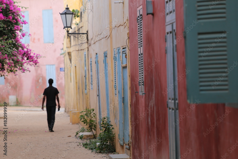 Silhouette of a lonely man walking in a narrow colored street of goree island in senegal - obrazy, fototapety, plakaty 