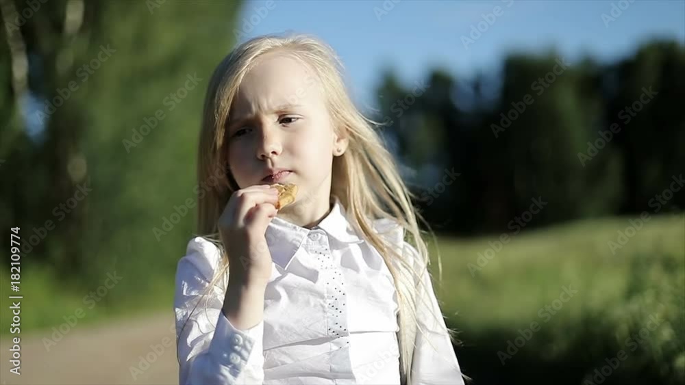 Hungry school girl in white shirt and black skirt is walking by the sandy road through the field and eats a biscuit. Hungry school girl in white shirt and black skirt is walking by the sandy road through the field and eats a biscuit.
