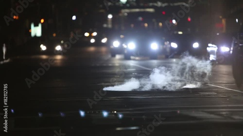 Steam coming out sewage at night while cars driving through