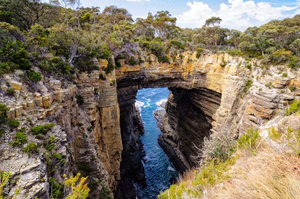 The huge solid rock bridge of the Tasman Arch  spans the gap across the chasm created by the wind and waves over millions of years - Eaglehawk Neck, Tasmania, Australia