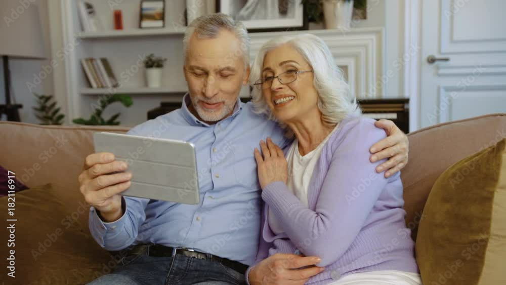 Portrait of grandparents sitting on the sofa at home and using tablet for video chatting. Close up shot. Portrait of grandparents sitting on the sofa at home and using tablet for video chatting. Close up shot.