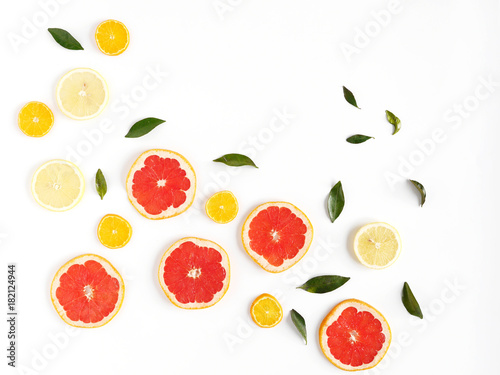 Pattern of fresh fruits on a white background  top view  flat lay.   Composition of green leaves and slices of citrus fruits  grapefruit  lemon  mandarin. Healthy food background  wallpaper  collage.