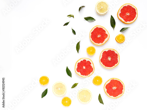 Pattern of fresh fruits on a white background, top view, flat lay. Composition of green leaves and slices of citrus fruits: grapefruit, lemon, mandarin. Healthy food background, wallpaper, collage.