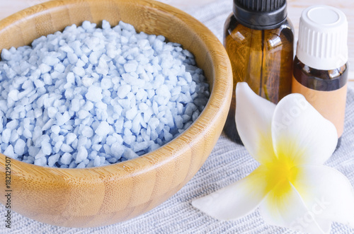 Blue spa sea salt en wooden bowl  essential oil and blue towel with exotic flower on wood background. Spa and wellness essential. Close up.