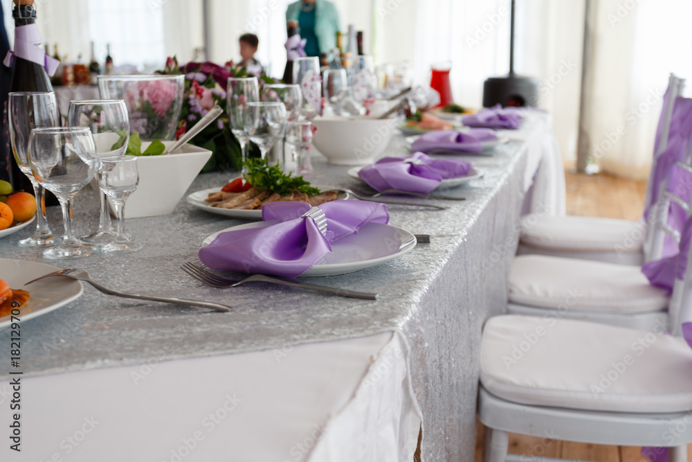 Served table plate with purple cloth. Wedding tables set for fine dining or another catered event. Napkin in the form of a bow. Plate, fork, knife on the background of the snacks on the table.