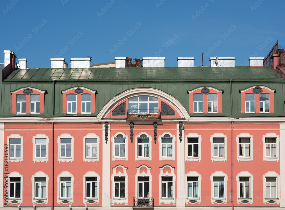 Facade of an old building with a mansard roof. Windows and pink walls. Green roof and blue sky