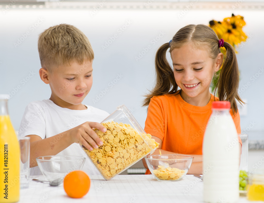 Brother pours a dry breakfast to his sister in the kitchen Brother pours a dry breakfast to his sister in the kitchen