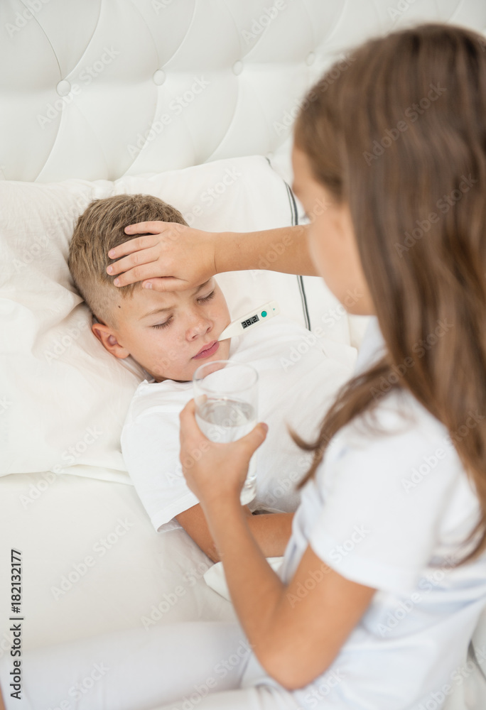 A girl with a glass of water touches her brother's forehead, checking the temperature A girl with a glass of water touches her brother's forehead, checking the temperature