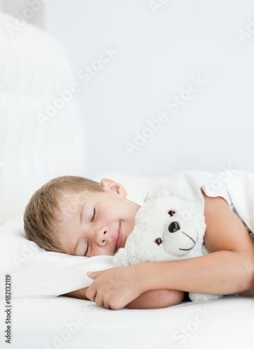 Happy boy sleeping in bed with toy bear