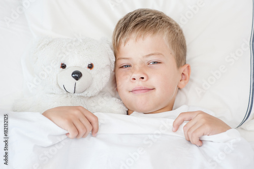 Little boy lying in bed with toy bear. Top view