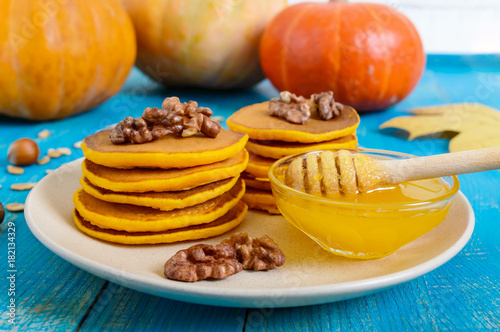 Fragrant golden pumpkin pancakes with honey and walnuts on a blue wooden background. Traditional American dish