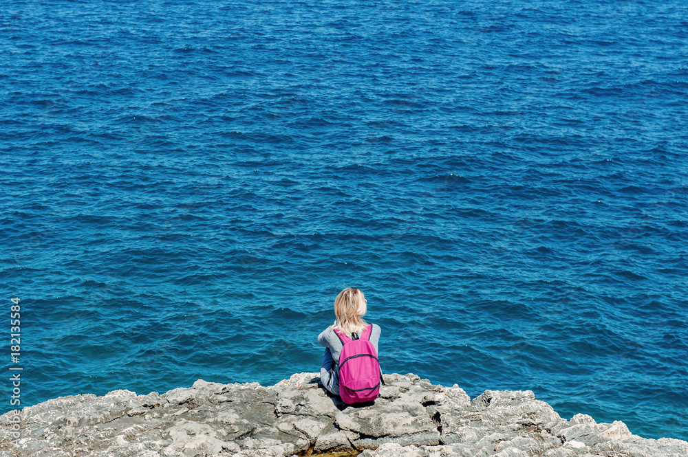 Woman tourist with backpack relaxing near blue sea in Polignano, Apulia, Italy