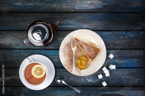 Slice of Cheesecake with jam rafinated sugar and tea kettle with lemon on a colored wooden background. Top view photo