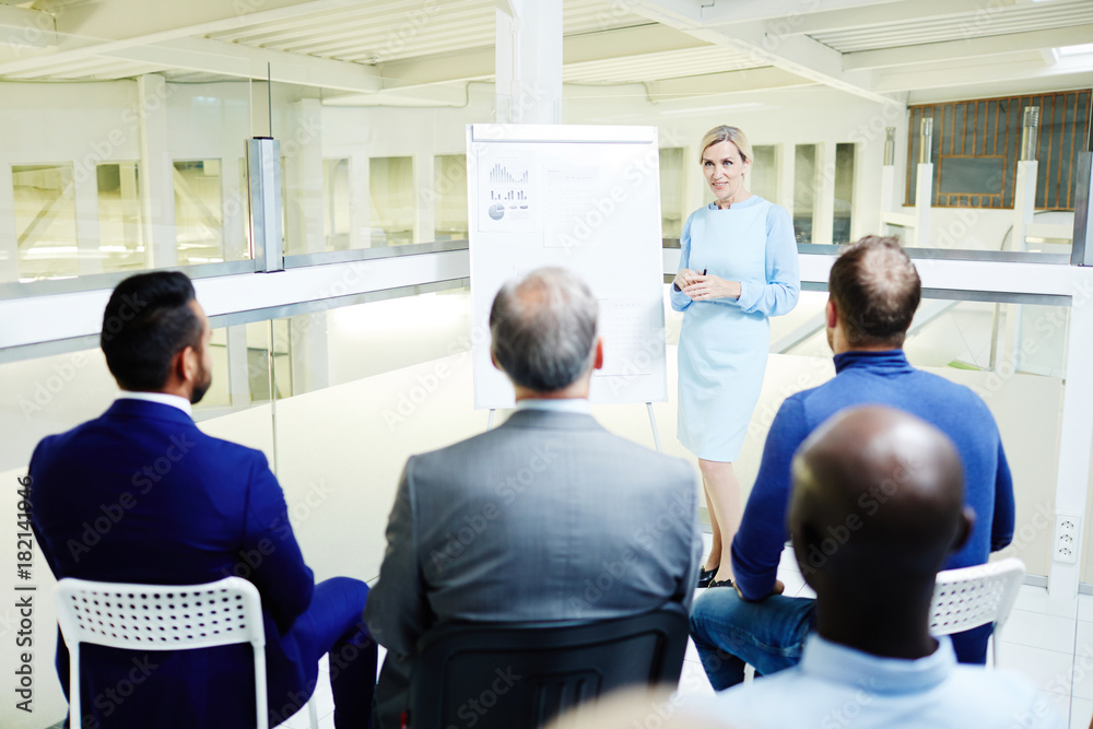 Confident financial expert standing by whiteboard and talking to audience at lecture Confident financial expert standing by whiteboard and talking to audience at lecture