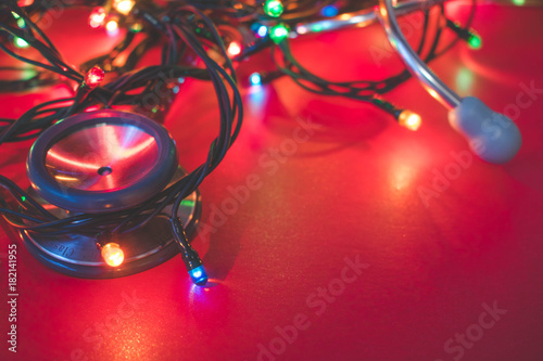 Close up view of a red stethoscope and shining colorful Christmas lights on red background, medical Christmas or happy holiday in hospital concept