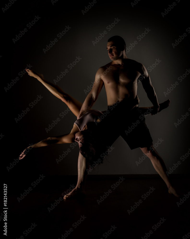 Young sports couple doing acroyoga exercises in a dark room