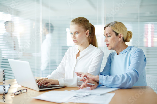 Mature employer explaining her young subordinate how to make report for conference