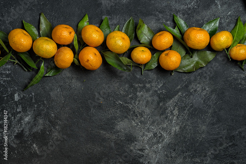 mandarines with leaves in a row on a black cement background with copy space for your text