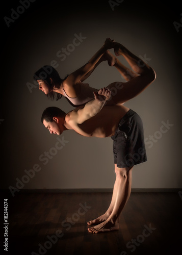 sports man and woman doing acroyoga exercises in a dark room