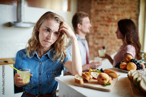 Angry young woman with drink expressing jealousy whiile her boyfriend talking to another girl at party photo