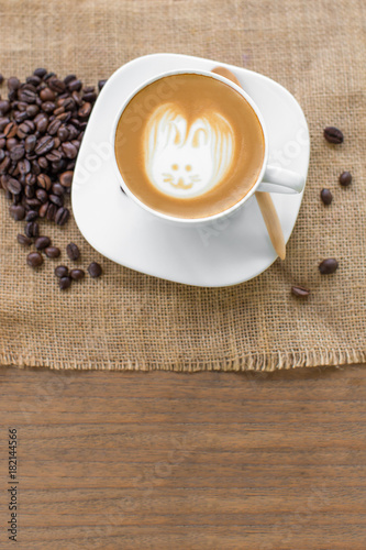 Easter rabbit drawing on latte art coffee cup. coffee in white cup and beans  on wood table. Free from copy space.