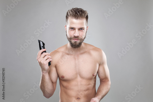 Portrait of young bearded man with a new hair cut, holdin a clipper