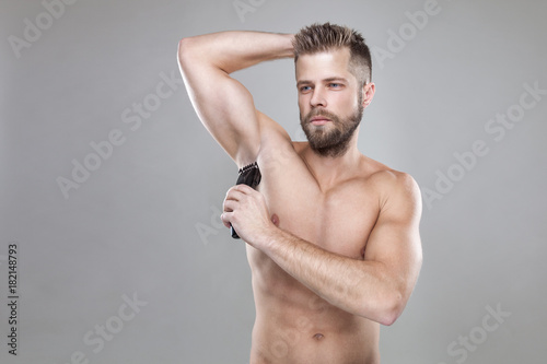 Handsome bearded man with a trimmer shaving off body hair photo