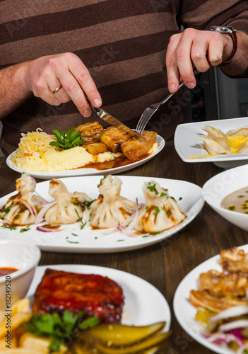 man hands with a knife and fork at a table with many different food