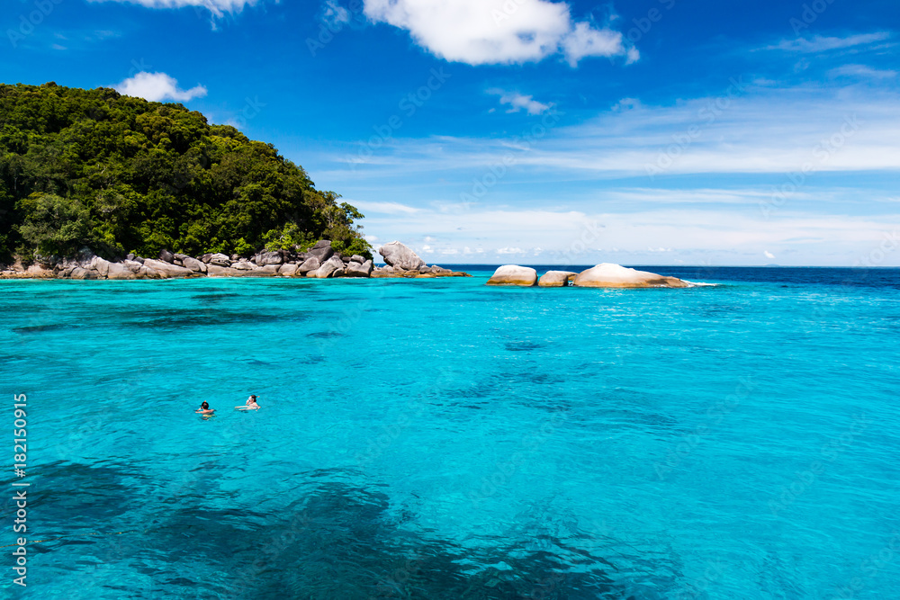 Snorkellers in clear tropical waters next to a remote, jungle covered island