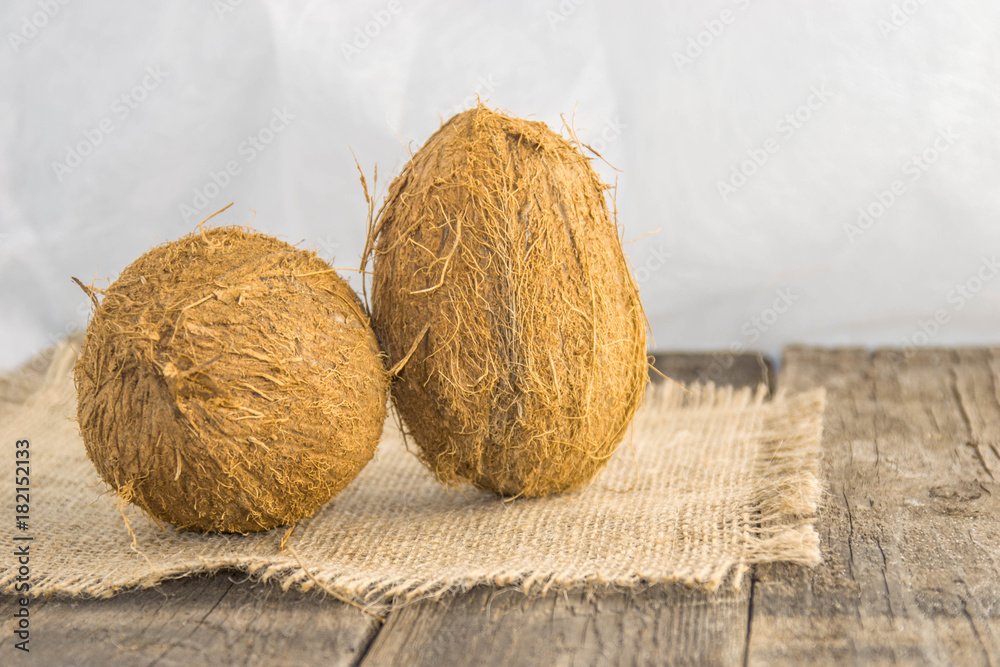 Coconut nuts, ripe, on a rustic jute base on a wooden table with a white background Coconut nuts, ripe, on a rustic jute base on a wooden table with a white background