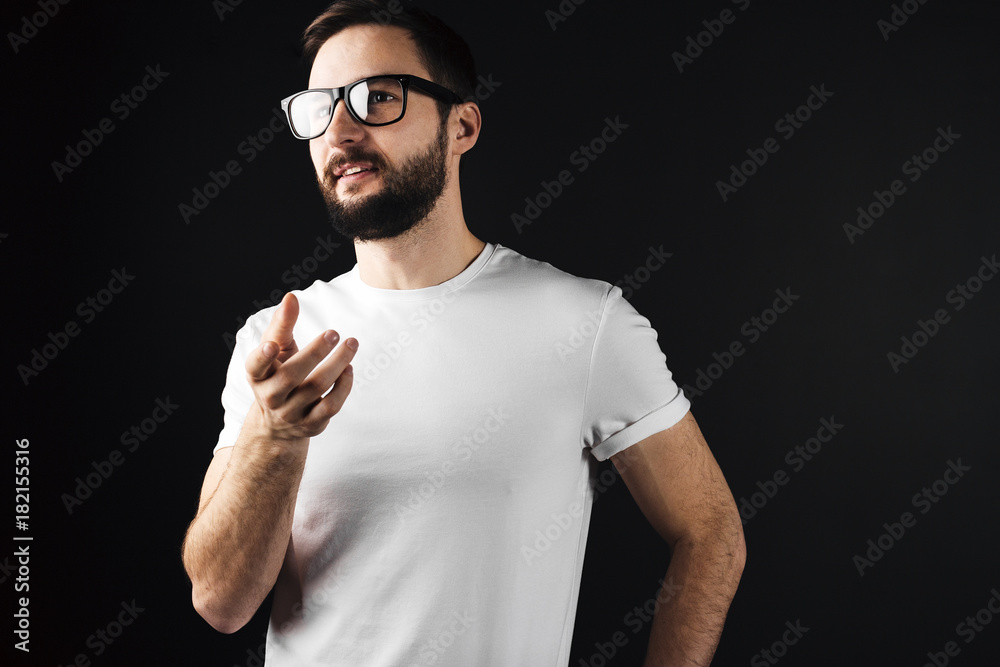 Handsome bearded young hipster wearing glasses and white bkank tshirt and shows something hand Handsome bearded young hipster wearing glasses and white bkank tshirt and shows something hand