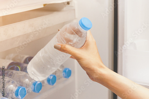 Hand of a girl taking out a water bottle or mineral water from refrigerator or a fridge on hotel or bed room or supermarket. Drinking water is beneficial to health.