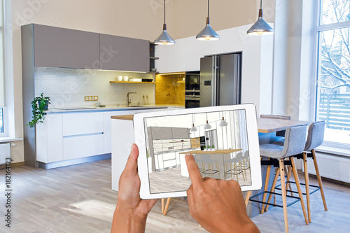 Hands holding tablet with kitchen interior sketch. In the background real finished kitchen interior design. Kitchen presentation. Home Interior Design Software Programs. Bar chairs.