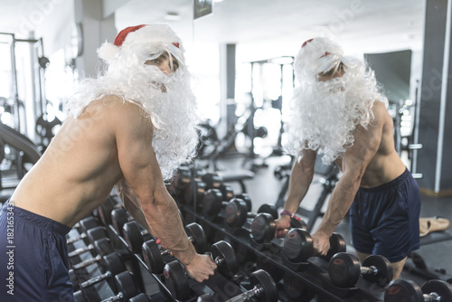 Fitness trainer ready for dumbbells exercises with santa claus cosume in christmas photo