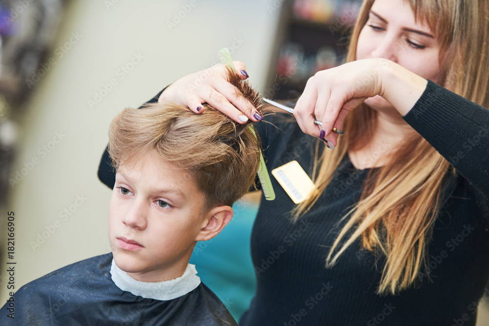 Naklejka premium Barber or hair stylist at work. female hairdresser cutting child hair