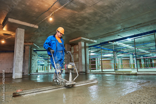 concrete floor construction. Worker with screeder photo