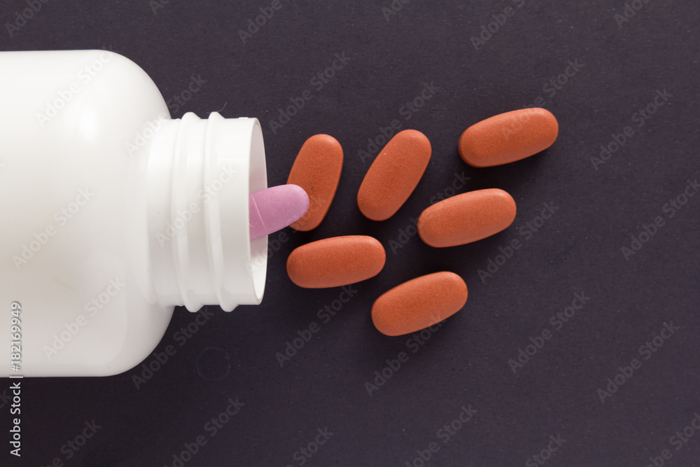 Capsules spilling out of white bottle. Black background. Capsules spilling out of white bottle. Black background.