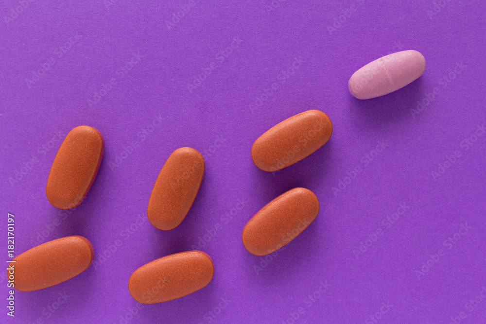 Heap of pills spreaded over color table. All tablets are red except one: pink Heap of pills spreaded over color table. All tablets are red except one: pink