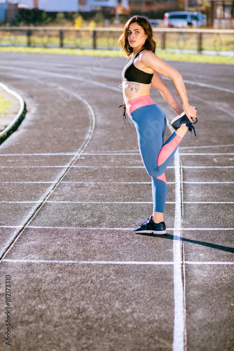 Vertical full body of sporty female jogger stretching on the track stadium. Warm up  morning running concept.