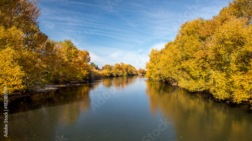 Fall trees line a river in Boise Idaho with blue sky