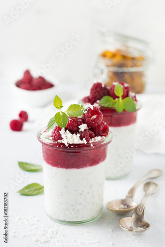Layered raspberry smoothies with chia seeds, fresh raspberry and coconut on a light stone background. Useful dessert. Selective focus.